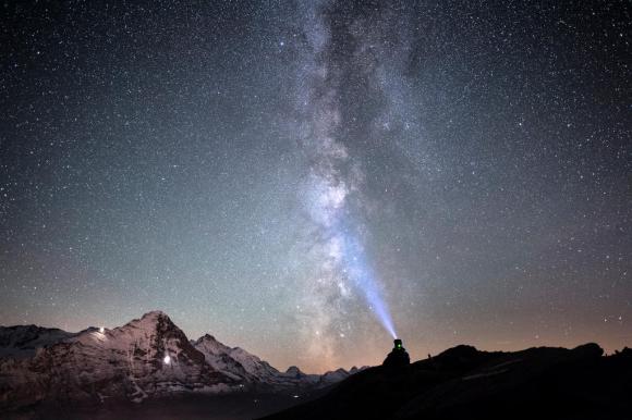 A man looks at the milky way with the Eiger mountain in the background
