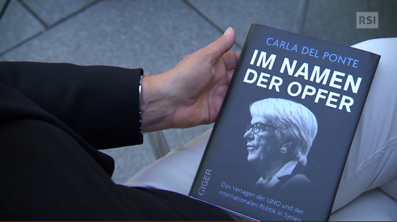 Carla Del Ponte mostra alla telecamera il libro, sul quale si appresta a scrivere una dedica
