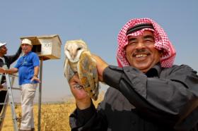 A Jordanian farmer holds a barn owl, while an Israeli farmer stands next to a nest box in the background