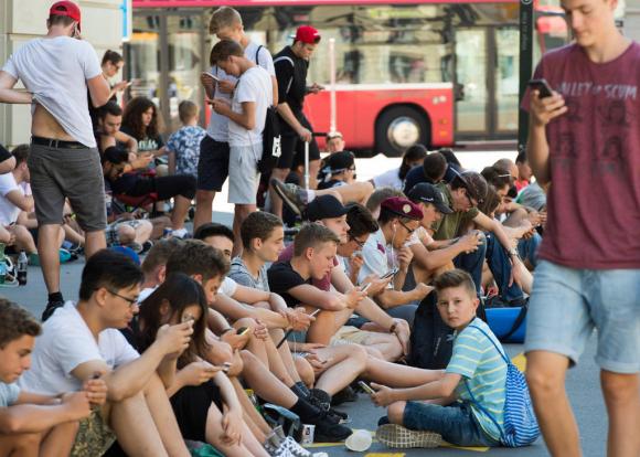 Junge Menschen sitzen vor einem Gebäude in der Stadt und schauen auf ihr Smartphone.