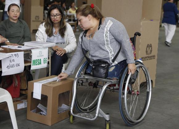 una donna con le gambe amputate, su una carrozzella, in un seggio elettorale mette una scheda nell urna.