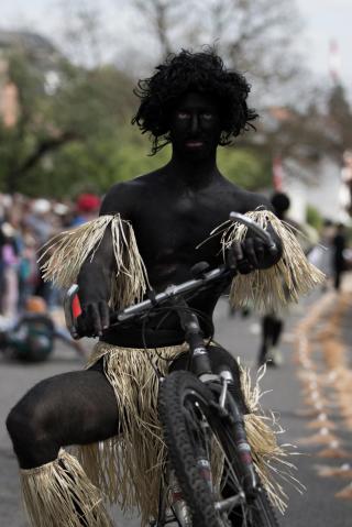 Hombre pintado de negro y con un tapa rabo a bordo montado en una bicicleta.