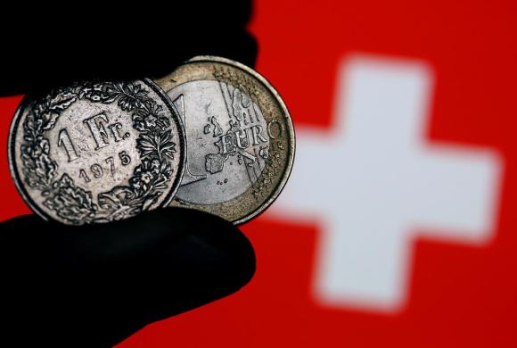 Fotografía de un franco y un euro y al fondo la bandera suiza.