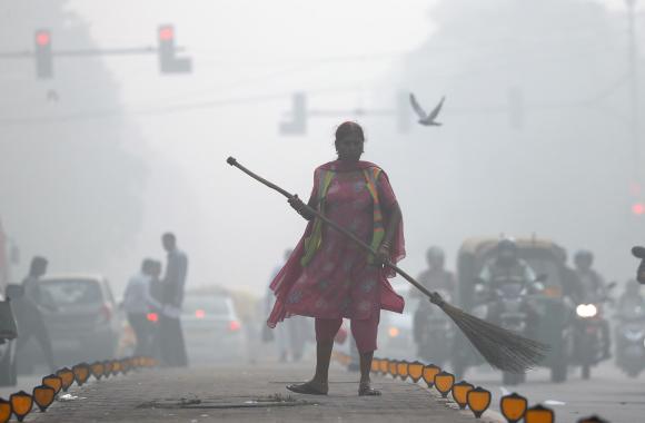 امرأة واقفة في أحد الشوارع حاملة لمكنسة وهي لا تكاد تُرى بسبب التلوث وكثافة الدخان
