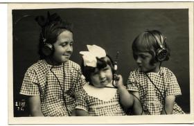 Três meninas com vestidos iguais e fones de ouvido, foto em preto e branco