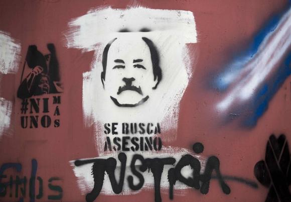 El rostro de Daniel Ortega, con el texto se busca asesino y un grafiti con la palabra jUSTICIA?. 