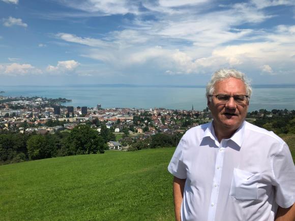Homem posando em cima de colina com uma cidade e lago ao fundo