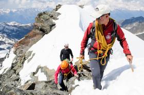 Tres alpinistas atados a una cuerda ascienden un pico nevado