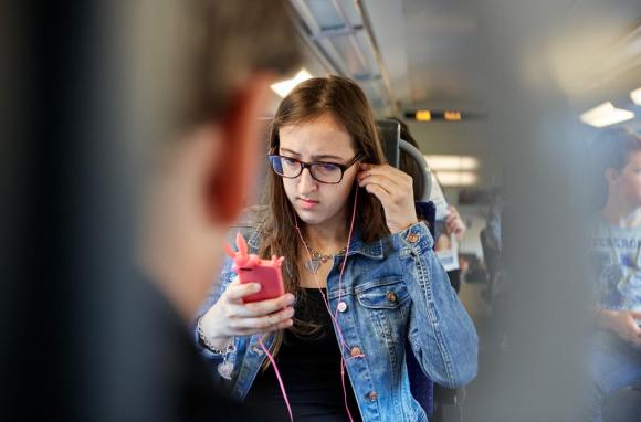 An adolescent commuter uses her mobile phone with plugged headphones