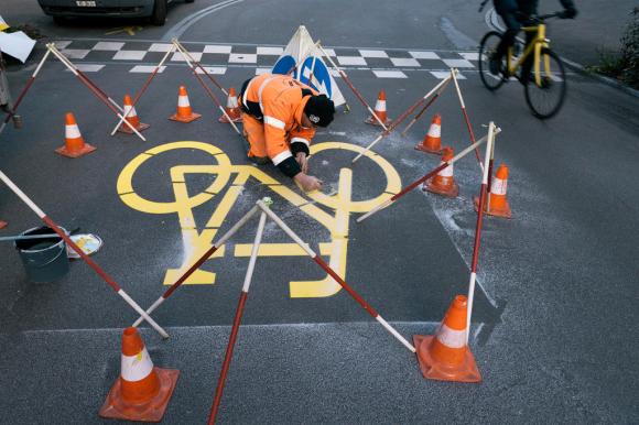 un operaio sta dipingendo su una corsia stradale il pittogramma simbolo delle ciclopiste.