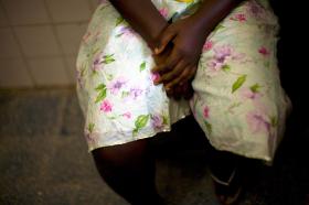Sitzende junge, afrikanische Frau mit geblümtem Rock und Händen in Schoss gelegt.