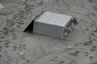 Metal rubbish container sunk in mud.