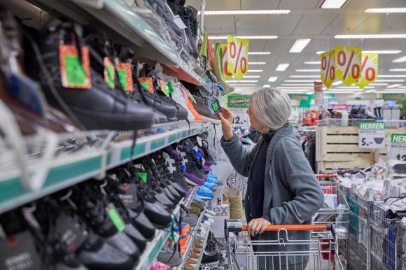 Betagte Frau sucht im Supermarkt für Schuhe die Preisangabe.