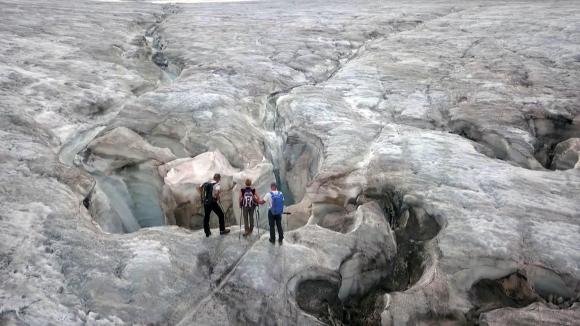 Three people standing at the edge of a glacier crevasse