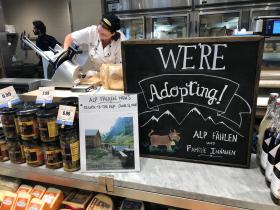 Woman slicing cheese behind a sign that says We re Adopting