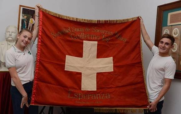 Jóvenes muestran la bandera de la Sociedad Suiza de Socorro en Esperanza, Argentina
