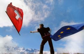 Hombre en el traje folclórico suizo izando una bandera suiza. En la otra sostiene la europea