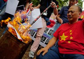 Homem com camisa da bandeira da China queima pôsteres