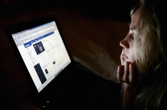 Frau schaut auf leuchtenden Computer-Bildschirm mit Facebook