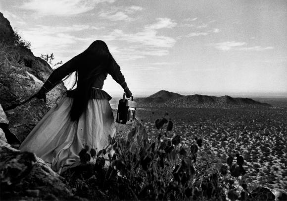 Back view of a woman with a veil carrying a ghettoblaster through a field