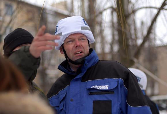 Ein Mann mit blauer Jacke und weissem Helm schaut in die Richtung, in die ein anderer Mann zeigt.