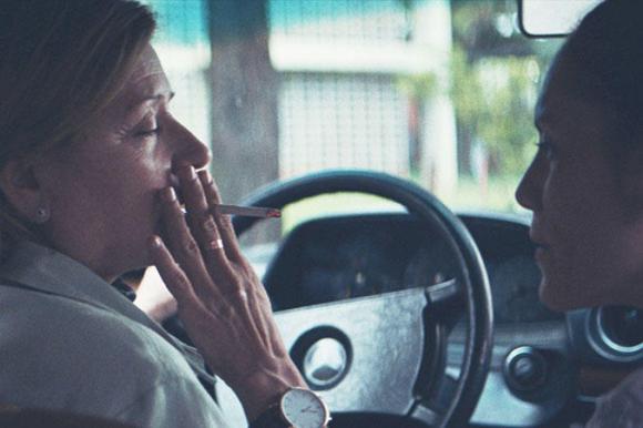 Dos mujeres sentadas al interior de un vehículo. Una fuma.