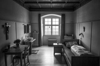 Klosterzelle mit schmalem Bett, Tisch, Stuhl, Lavabo und Fenster