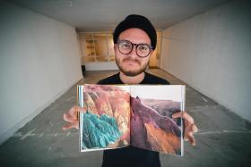 Ein junger Mann mit Brille zeigt ein Fotobuch