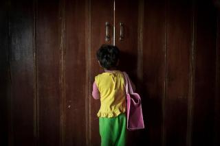 Una niña de espaldas a la cámara mira por el espacio de una puerta entreabierta