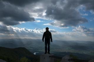 A person stands with their back to the camera. Looking towards a dramatic sky and landscape.