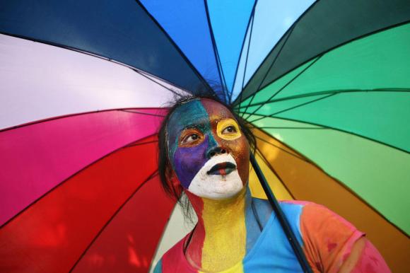 A woman with a painted face underneath a rainbow umbrella