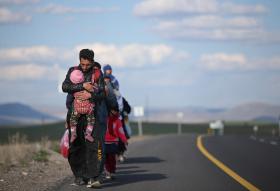 Migrantes (adultos y niños) caminan sobre una carretera.