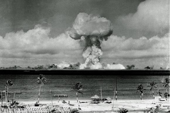 Mushroom cloud of an atom bomb rises among abandoned ships in Bikini lagoon.