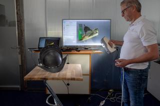 A man scans a helmet which is standing on a table, with a computer screen in the background.
