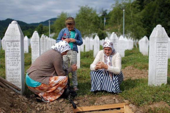 ثلاث نساء مجتمعات حول نصب تذكاري في مقبرة لضحايا مذبحة سريبرينيتشا في جمهورية البوسنة