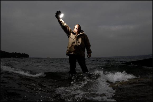 Jean Revillard a la orilla del mar, en la noche y con una linterna en la mano en alto dirigida hacia sí mismo.
