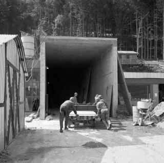 Workmen pushing a trailer into entrance of a mountainside.