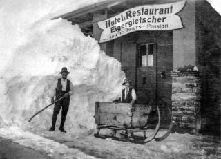 雪に半分埋まったレストランの前に立つ二人の男性