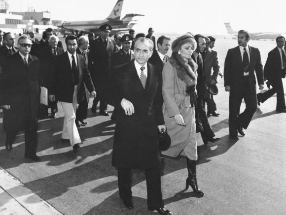 Ein Mann und eine Frau auf einem Flughafen, begleitet von einer Gruppe Männer.