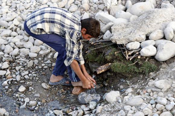 Un niño se lava los pies con el agua que sale de un tubo entre las piedras