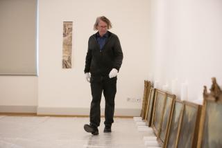 Peter Fischer geht entlang von mehreren am Boden stehenden Gemälden.