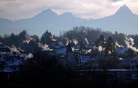 Sicht übers Mittelland auf die Berge, im Vordergrund viel Rauch aus Kaminen
