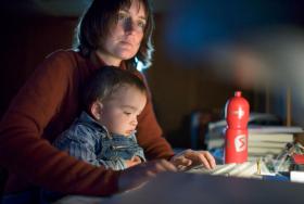 молодая женщина в темноте за компьютером с ребенком на коленях
