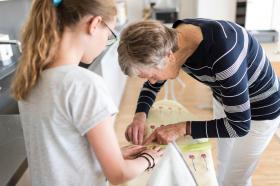 Eine Rentnerin hilft einem jungen Mädchen beim Nähen