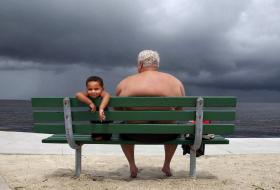 Un hombre de cierta edad con un niño menor en una banca frenta a una playa