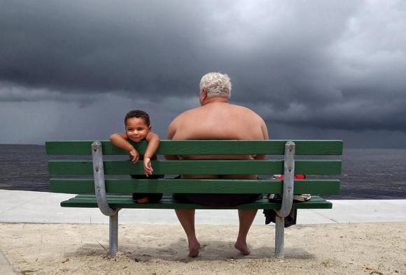 Alter Vater sitzt mit kleinem Kind auf einer Bank an einem Strand
