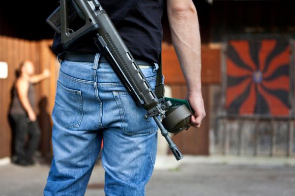 Un hombre de espaldas con un fusil de asalto colgado