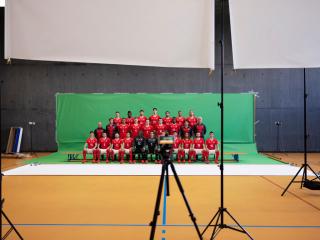 赤いユニフォームを着て整列し写真を撮るサッカー選手たち