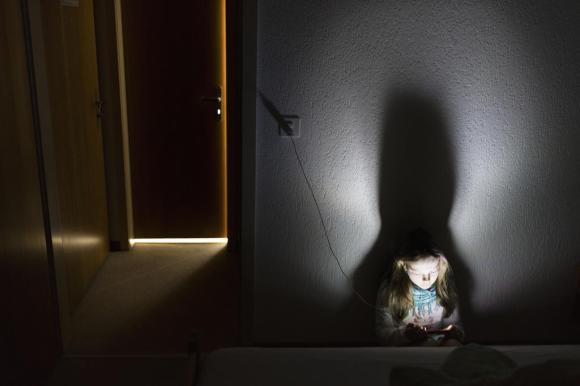 En una sala obscura, una niña consulta un teléfono inteligente