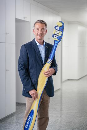 CEO Adrian Pfenniger mit einer mannshohen Zahnbürste im Arm